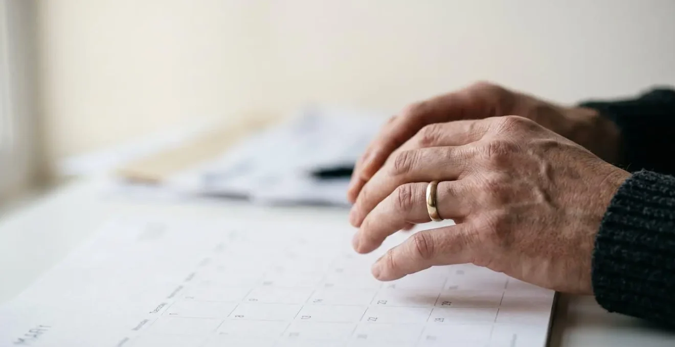 Close-up of hands marking calendar dates with financial planning materials showing time-sensitive decision making